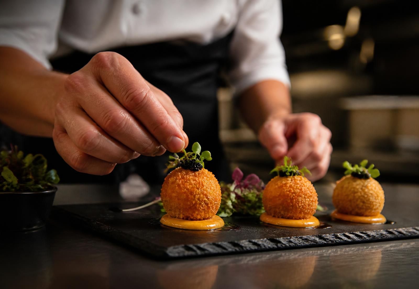 Manos elaborando croquetas artesanales en una cocina profesional